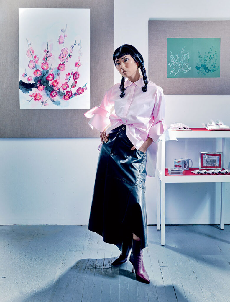 Mika Horibuchi wearing Loewe leather skirt, and cotton and silk shirt with double cuffs, and Simone Rocha glass- and brass-beaded earrings, and Jimmy Choo Cycas nappa leather ankle boots